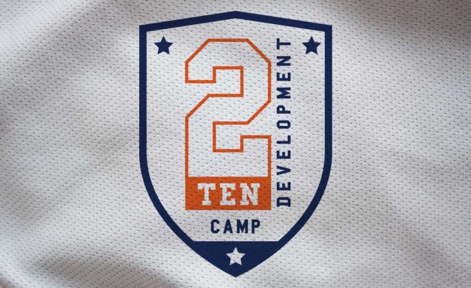 2Ten Camp Identity - 2 Ten Development Camp logo on a textured fabric background featuring a shield design with a bold number 2, orange and navy blue accents, and stars for decorative elements.