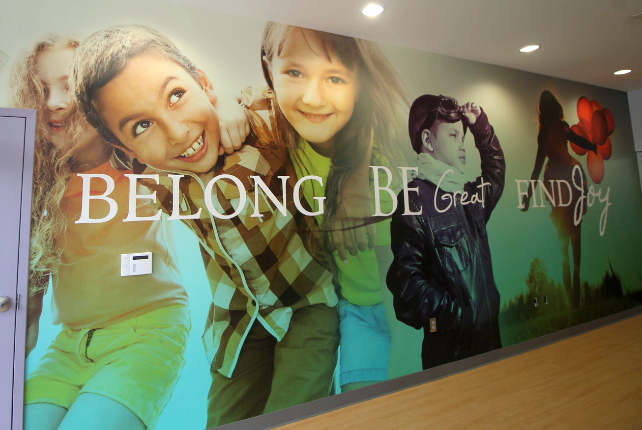 Anne Frank Inspire Academy: Elementary - A wall mural featuring images of happy children and the words "BELONG," "BE Great," and "FIND Joy