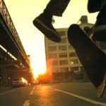 Action shot of a skateboarder performing a trick mid-air on an urban street during sunset.