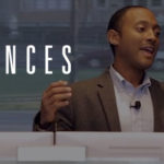 A man wearing a suit gestures confidently while speaking behind a podium with the word ‘CHANCES’ overlayed in bold white text.