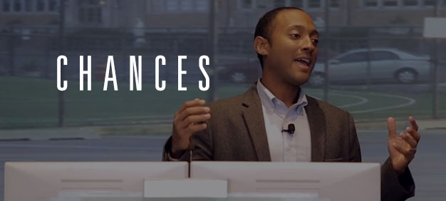 A man wearing a suit gestures confidently while speaking behind a podium with the word ‘CHANCES’ overlayed in bold white text.