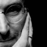 Steve Jobs - Close-up black-and-white portrait of a man wearing glasses, resting his face on his hand, looking thoughtful