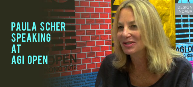 Paula Scher speaking at the AGI Open event, featuring vibrant, colorful design elements in the background.