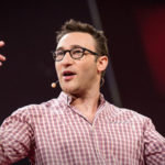 Speaker passionately addressing an audience during a presentation, wearing a checkered shirt and a microphone headset