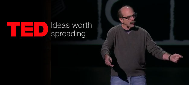 Speaker presenting on stage at a TED talk, with the TED logo and tagline ‘Ideas worth spreading’ displayed