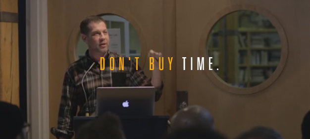 Speaker presenting at a seminar with the text overlay ‘Don’t Buy Time’ emphasizing a motivational message.