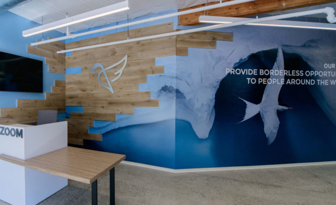 INSZoom Office – California - INSZoom office lobby with a modern wooden accent wall, branded bird logo, and a mural emphasizing the vision of providing borderless opportunities to people worldwide.