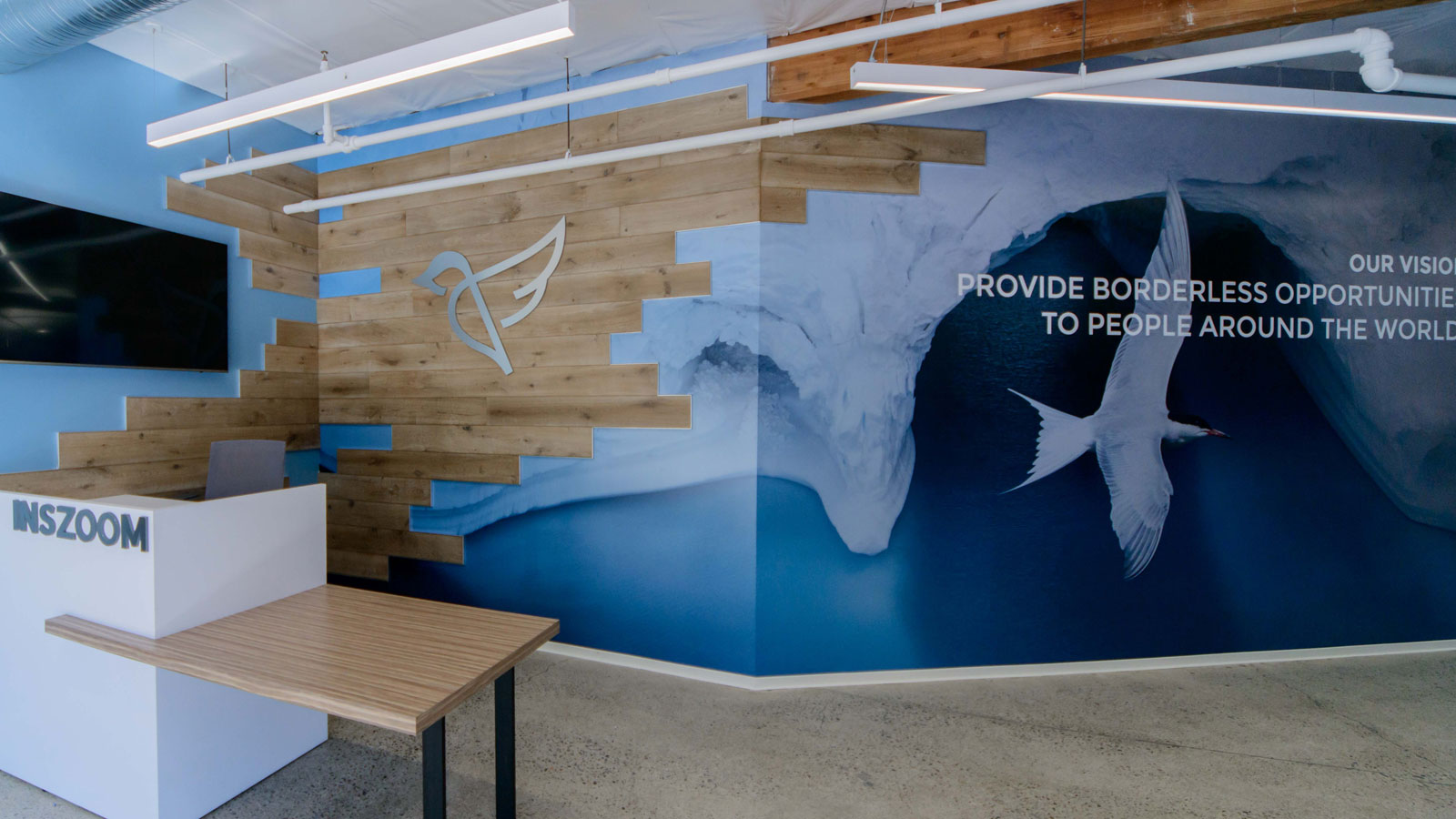 INSZoom Office – California - INSZoom office lobby with a modern wooden accent wall, branded bird logo, and a mural emphasizing the vision of providing borderless opportunities to people worldwide.