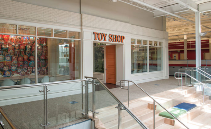 Toy Shop Rackspace San Antonio - Interior of a modern toy shop with large glass windows showcasing colorful matryoshka dolls, featuring sleek railings and a staircase in a bright and open space