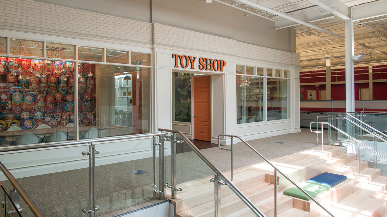 Toy Shop Rackspace San Antonio - Interior of a modern toy shop with large glass windows showcasing colorful matryoshka dolls, featuring sleek railings and a staircase in a bright and open space