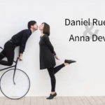 Daniel Rueda and Anna Devis creatively posing with a bicycle against a minimalist white background.