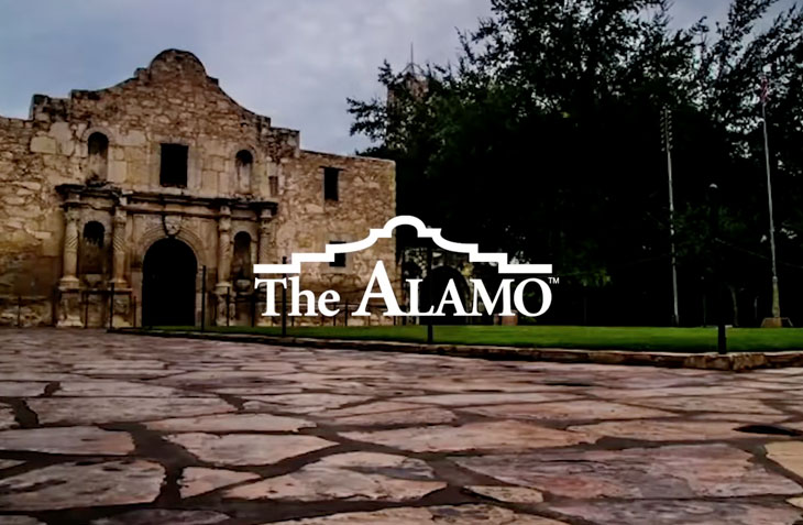 The Vault: The Alamo -Our Work - This is an image of the iconic Alamo, featuring its historic stone facade, with "The Alamo" logo prominently displayed. The setting highlights the paved courtyard and surrounding greenery, emphasizing the landmark's cultural and historical significance.