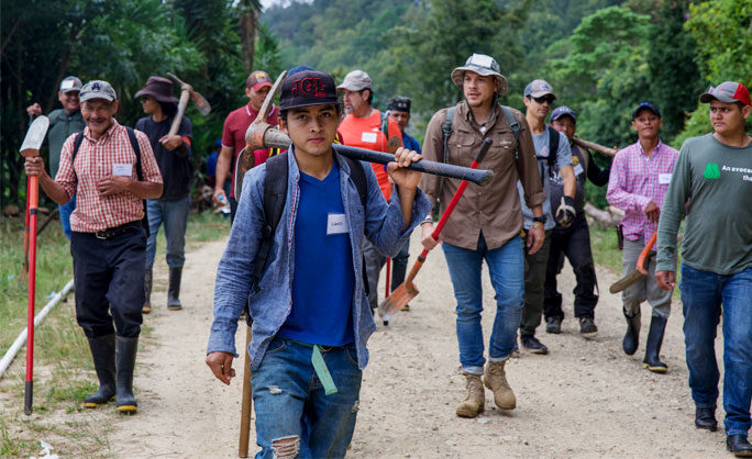 a group of people walking on a dirt path with axes